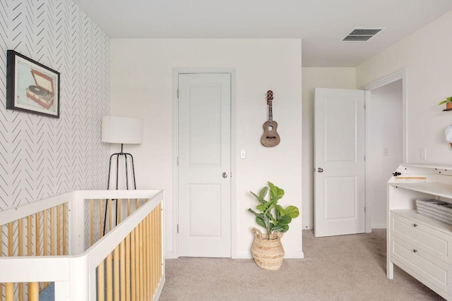 bedroom with a nursery area, light colored carpet, an accent wall, wallpapered walls, and visible vents