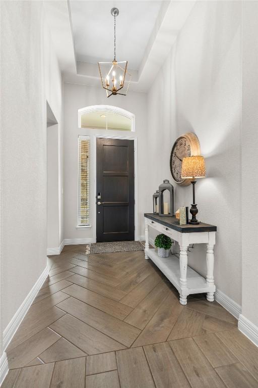 foyer entrance featuring baseboards, a raised ceiling, and a notable chandelier