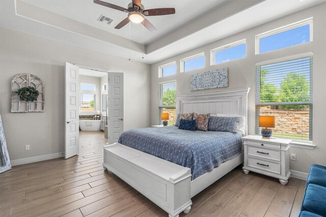 bedroom with visible vents, a raised ceiling, light wood-style flooring, and baseboards