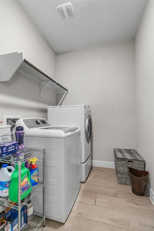 laundry room featuring laundry area, visible vents, baseboards, washing machine and clothes dryer, and light wood finished floors