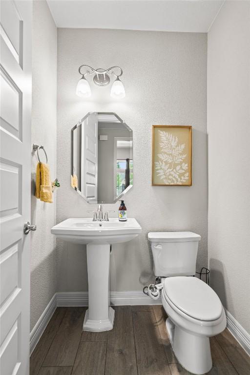half bath featuring a sink, baseboards, toilet, and wood finished floors