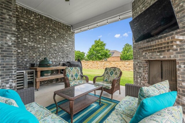 view of patio / terrace with an outdoor living space with a fireplace, wine cooler, ceiling fan, grilling area, and a fenced backyard