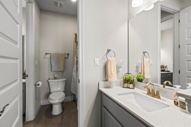 bathroom with vanity, toilet, a shower with shower curtain, wood finished floors, and visible vents