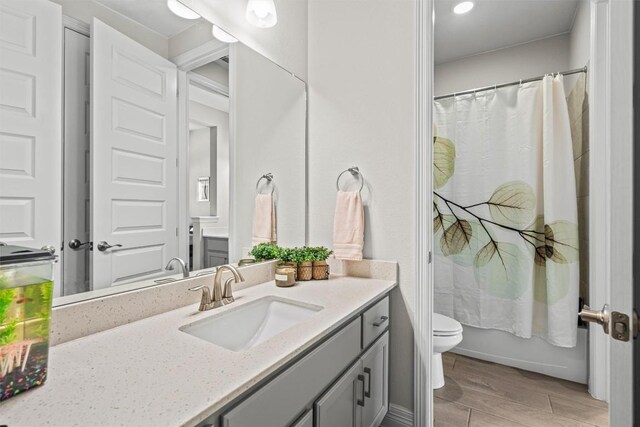 bathroom with vanity, wood finished floors, toilet, and shower / bath combo with shower curtain