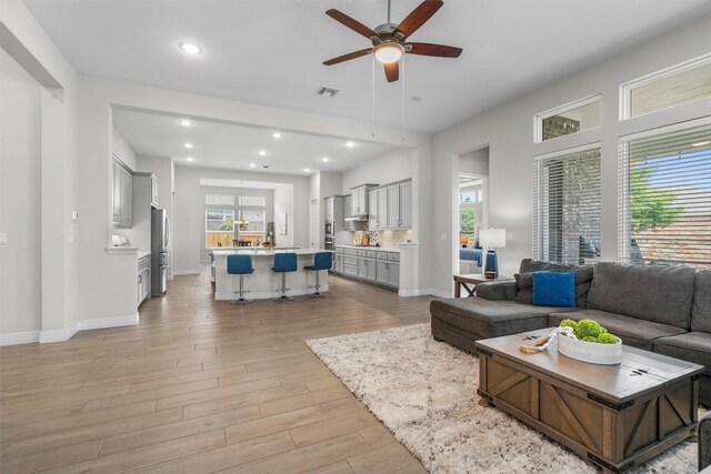 living room with ceiling fan, visible vents, baseboards, light wood-style floors, and recessed lighting