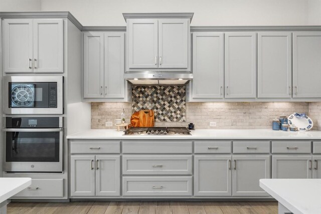 kitchen with under cabinet range hood, stainless steel appliances, gray cabinetry, and light countertops