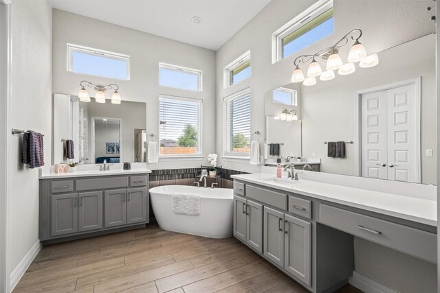 bathroom with a sink, a high ceiling, wood finished floors, and a soaking tub