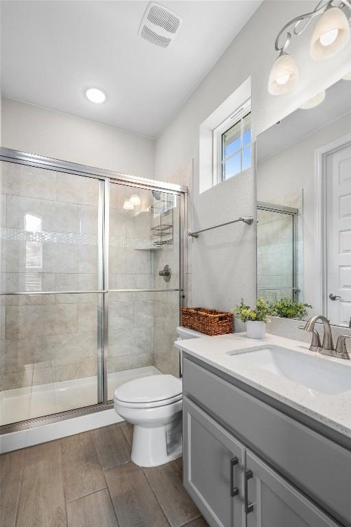 bathroom featuring visible vents, vanity, wood finished floors, toilet, and a shower stall