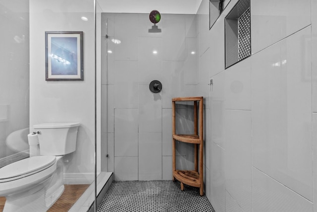 bathroom featuring toilet, tiled shower, and tile patterned flooring