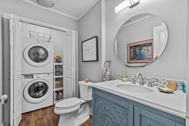 bathroom featuring vanity, ornamental molding, wood finished floors, toilet, and stacked washing maching and dryer