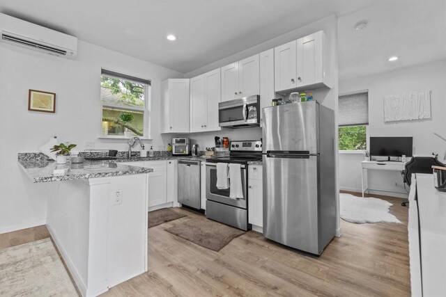 kitchen featuring a peninsula, a wall mounted air conditioner, white cabinetry, stone counters, and appliances with stainless steel finishes