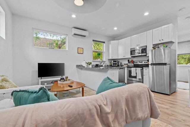 living room featuring recessed lighting, light wood-type flooring, plenty of natural light, and a wall mounted air conditioner