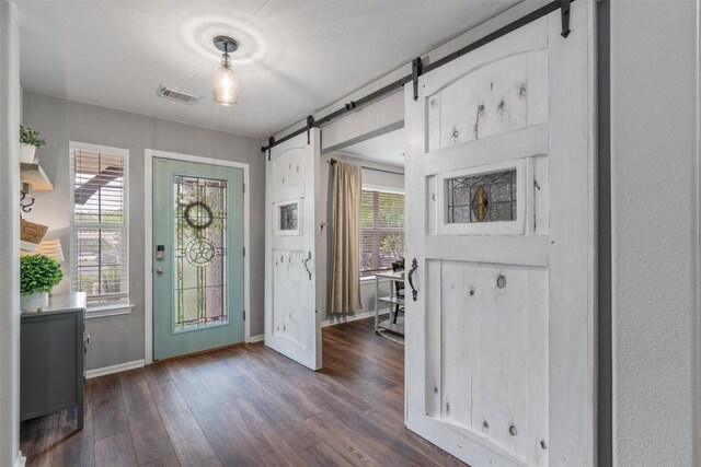 foyer entrance featuring visible vents, a barn door, dark wood-type flooring, and a healthy amount of sunlight