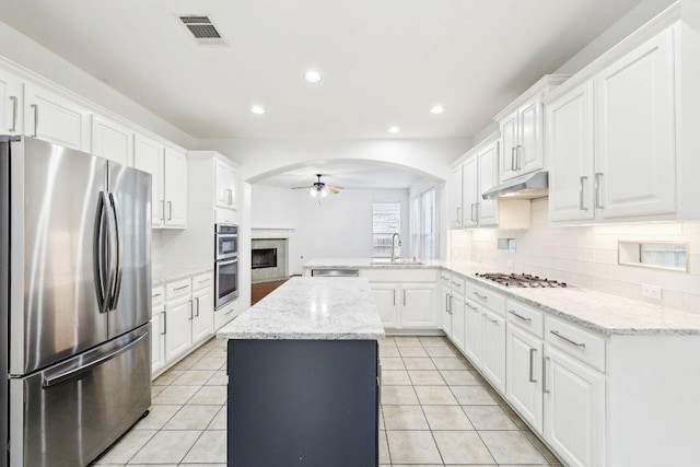 kitchen featuring ceiling fan, appliances with stainless steel finishes, a fireplace, a sink, and a peninsula