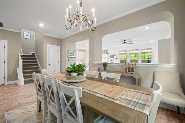 dining room with crown molding, arched walkways, wood finished floors, ceiling fan with notable chandelier, and recessed lighting