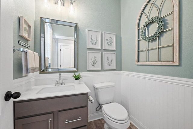 bathroom with a wainscoted wall, vanity, toilet, and wood finished floors
