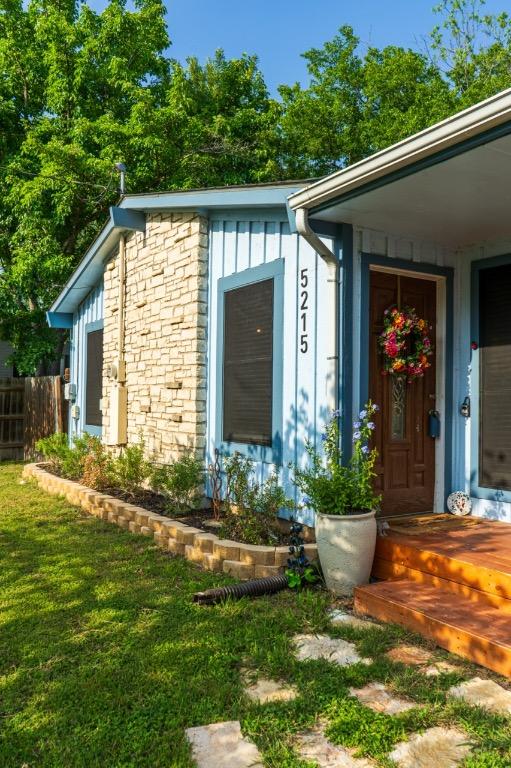 view of exterior entry with board and batten siding, fence, and a yard