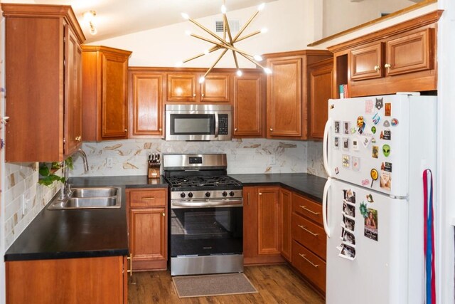 kitchen featuring decorative backsplash, appliances with stainless steel finishes, dark countertops, a sink, and an inviting chandelier
