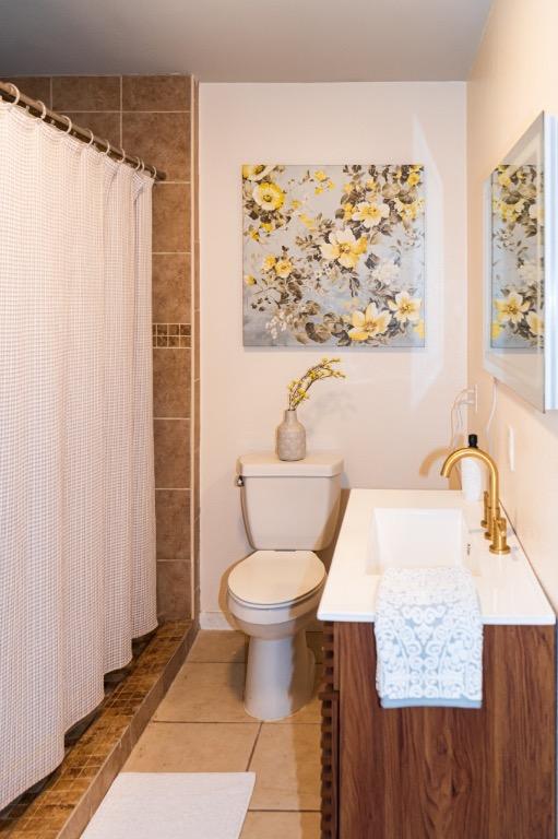 bathroom with tile patterned flooring, tiled shower, toilet, and vanity