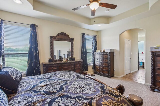 bedroom featuring arched walkways, a tray ceiling, multiple windows, and carpet