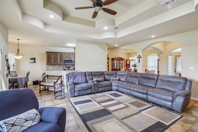 living room featuring arched walkways, ceiling fan with notable chandelier, recessed lighting, a tray ceiling, and visible vents