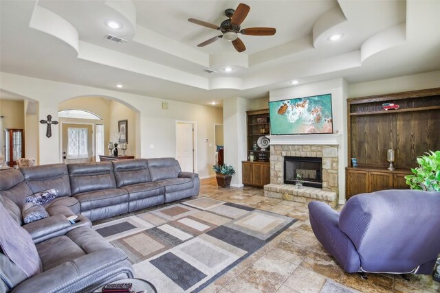 living area featuring a ceiling fan, a fireplace, recessed lighting, a raised ceiling, and arched walkways