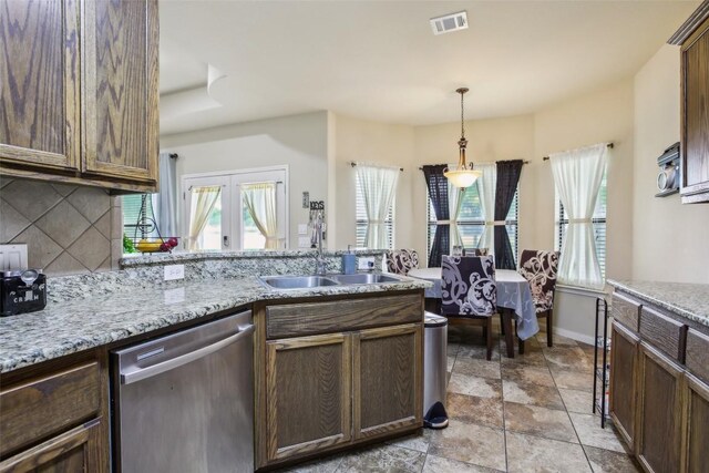kitchen featuring a sink, stone finish floor, backsplash, stainless steel dishwasher, and visible vents