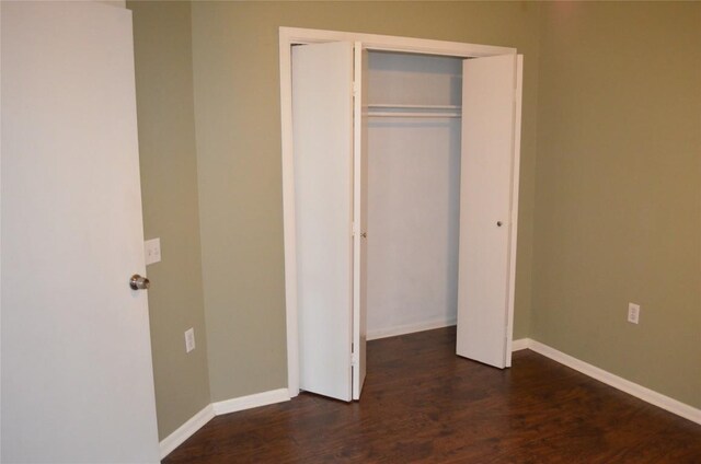 unfurnished bedroom with dark wood-style flooring, baseboards, and a closet