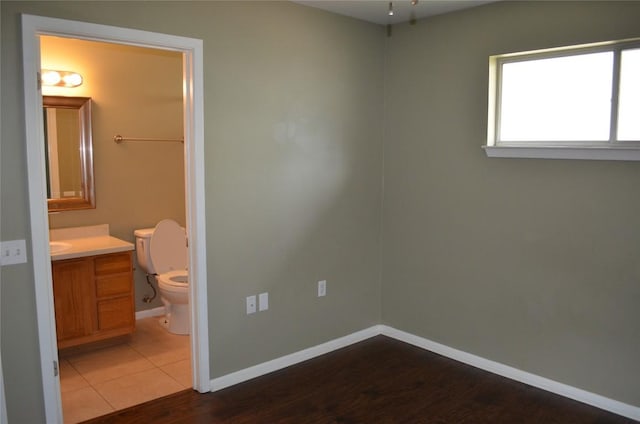 5009 Lott Ave, Austin, TX 78721 - unfurnished bedroom with connected bathroom, an office area, baseboards, and wood finished floors