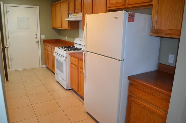 kitchen with light tile patterned floors, under cabinet range hood, and white appliances