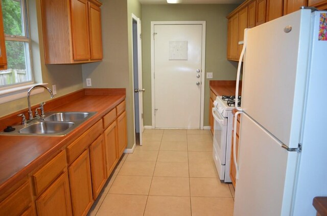 kitchen featuring brown cabinets, a sink, light tile patterned floors, baseboards, and white appliances