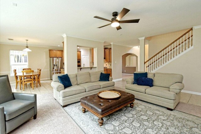 living area featuring crown molding, stairs, baseboards, ceiling fan, and arched walkways