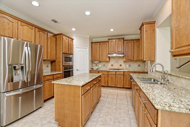 kitchen with a sink, light stone counters, under cabinet range hood, ornamental molding, and stainless steel appliances