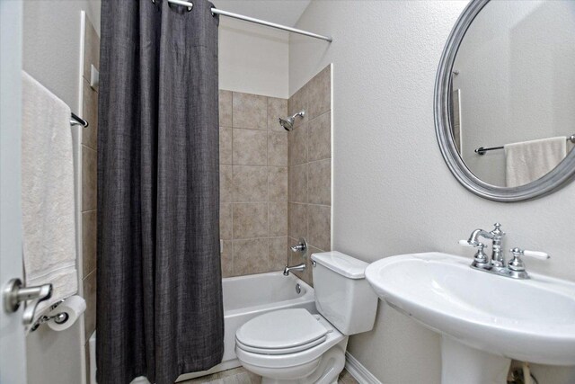 bathroom featuring toilet, shower / bath combination with curtain, and a sink
