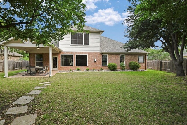 rear view of house with brick siding, a fenced backyard, a lawn, and a patio