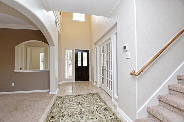 carpeted foyer with tile patterned flooring, arched walkways, stairs, baseboards, and ornamental molding