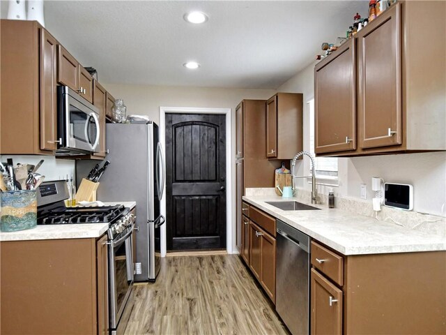 kitchen with appliances with stainless steel finishes, a sink, light countertops, recessed lighting, and light wood-style flooring