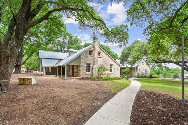 rear view of house with a lawn, a chimney, metal roof, and stone siding