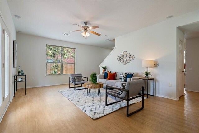 living room featuring light wood-type flooring, baseboards, ceiling fan, and visible vents