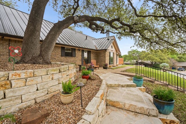 view of home's exterior featuring a standing seam roof, fence, metal roof, and brick siding