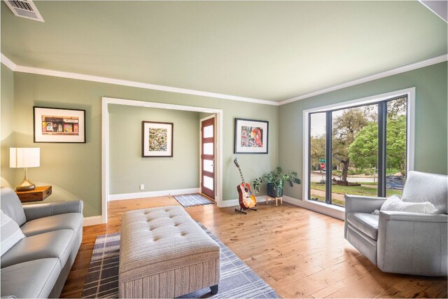 living area featuring baseboards, visible vents, ornamental molding, and light wood-type flooring