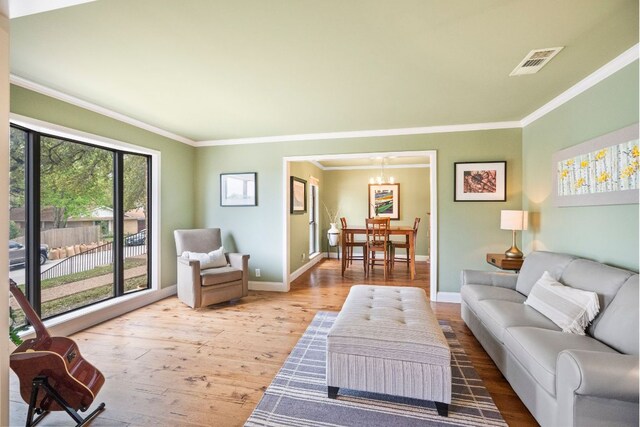 living area with visible vents, crown molding, wood finished floors, baseboards, and a chandelier