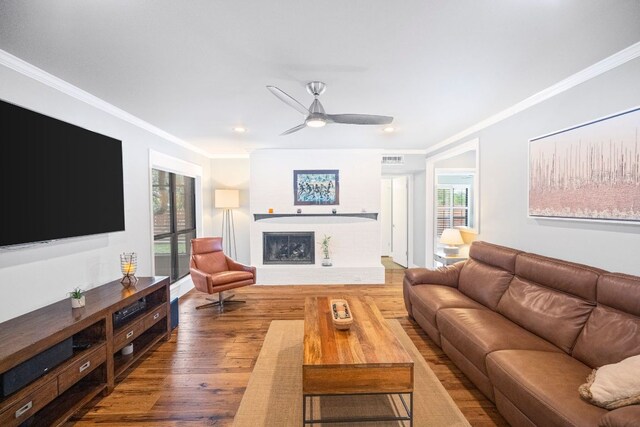 living area with crown molding, plenty of natural light, a fireplace, and wood finished floors