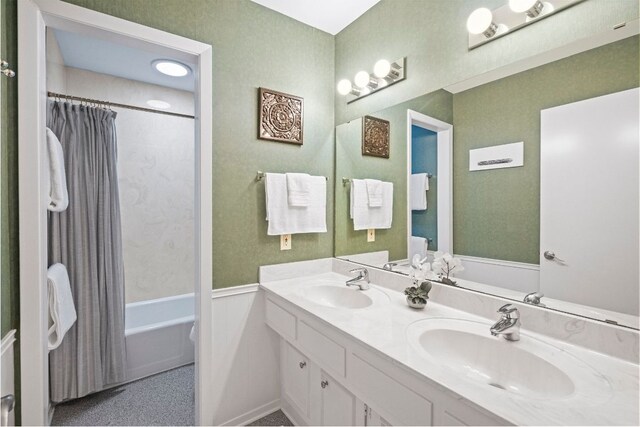 bathroom with a wainscoted wall, double vanity, a sink, and shower / tub combo
