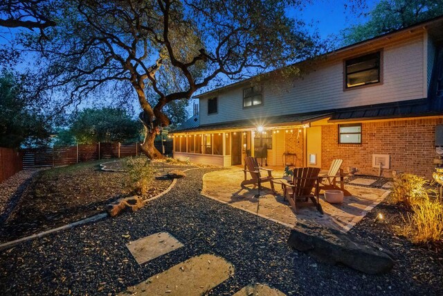 back of house with a standing seam roof, metal roof, brick siding, fence, and a patio