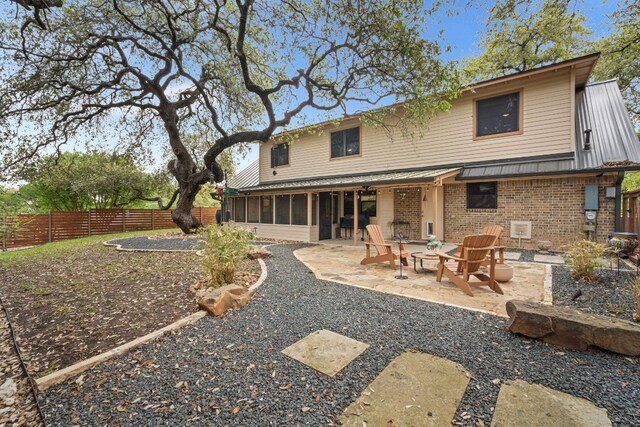 back of house featuring brick siding, a sunroom, a fenced backyard, a patio, and a fire pit