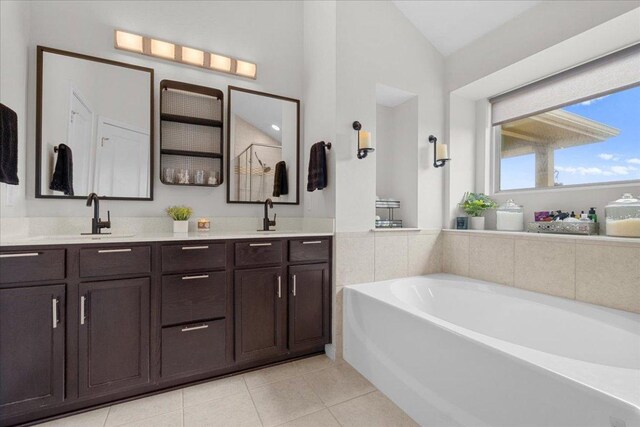 bathroom with tile patterned flooring, double vanity, a garden tub, lofted ceiling, and a sink