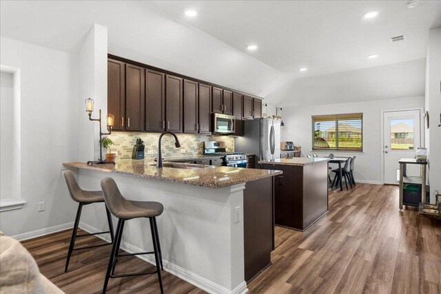 kitchen with a kitchen island, appliances with stainless steel finishes, dark brown cabinets, a sink, and light stone counters