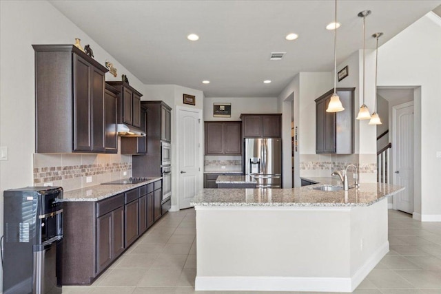 1800 Erie Dr, Leander, TX 78641 - kitchen featuring appliances with stainless steel finishes, dark brown cabinetry, light tile patterned flooring, under cabinet range hood, and light stone countertops