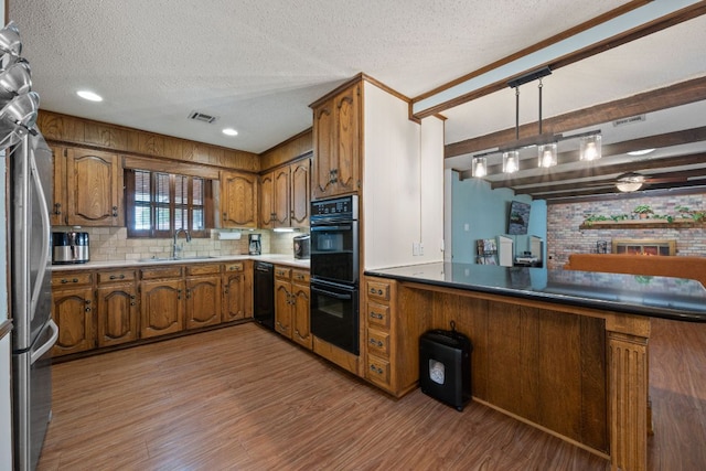 3909 Alderwood Ln, Temple, TX 76502 - kitchen with brown cabinets, black appliances, light wood-type flooring, a textured ceiling, and backsplash